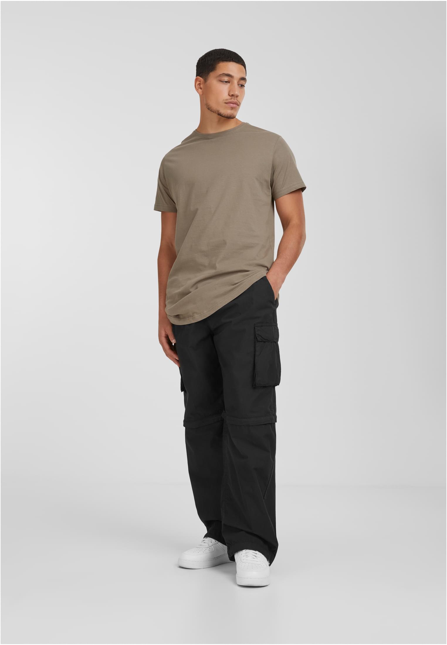 En manlig modell som bär en ljusbrun Shaped Long Tee med rundad fåll, svarta cargobyxor och vita sneakers mot en ljusgrå bakgrund.