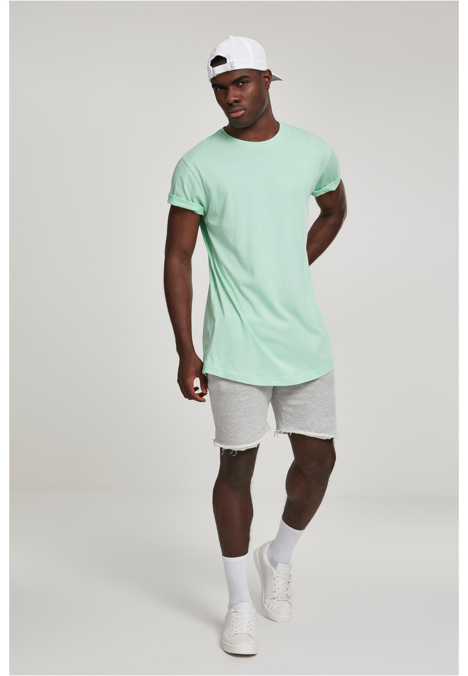 Manlig modell som bär en mintgrön UC Shaped Long Tee, stylad med grå shorts och en vit keps.