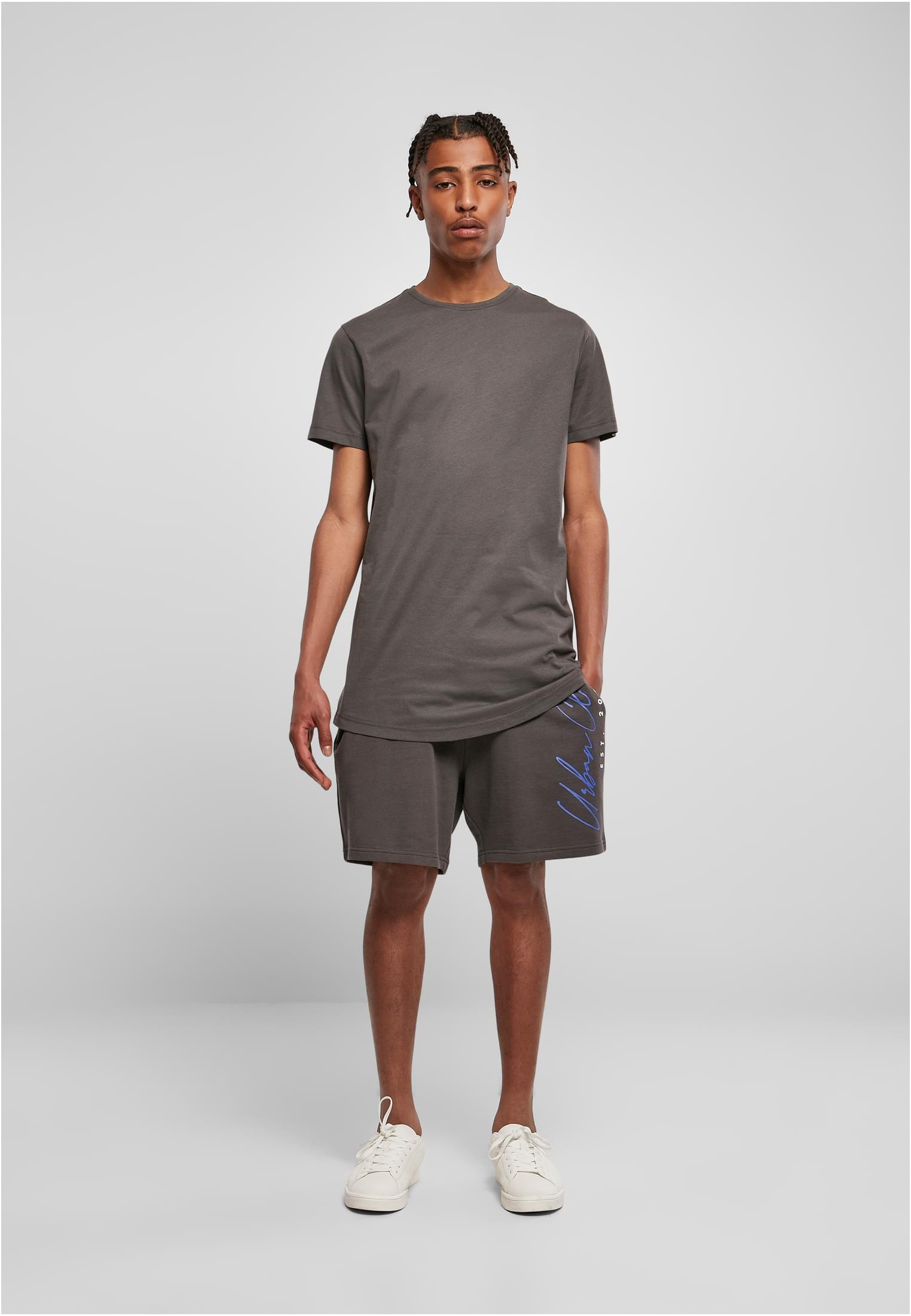 Manlig modell som bär en mörkgrå UC Shaped Long Tee, matchande shorts och vita sneakers, fotograferad framifrån.