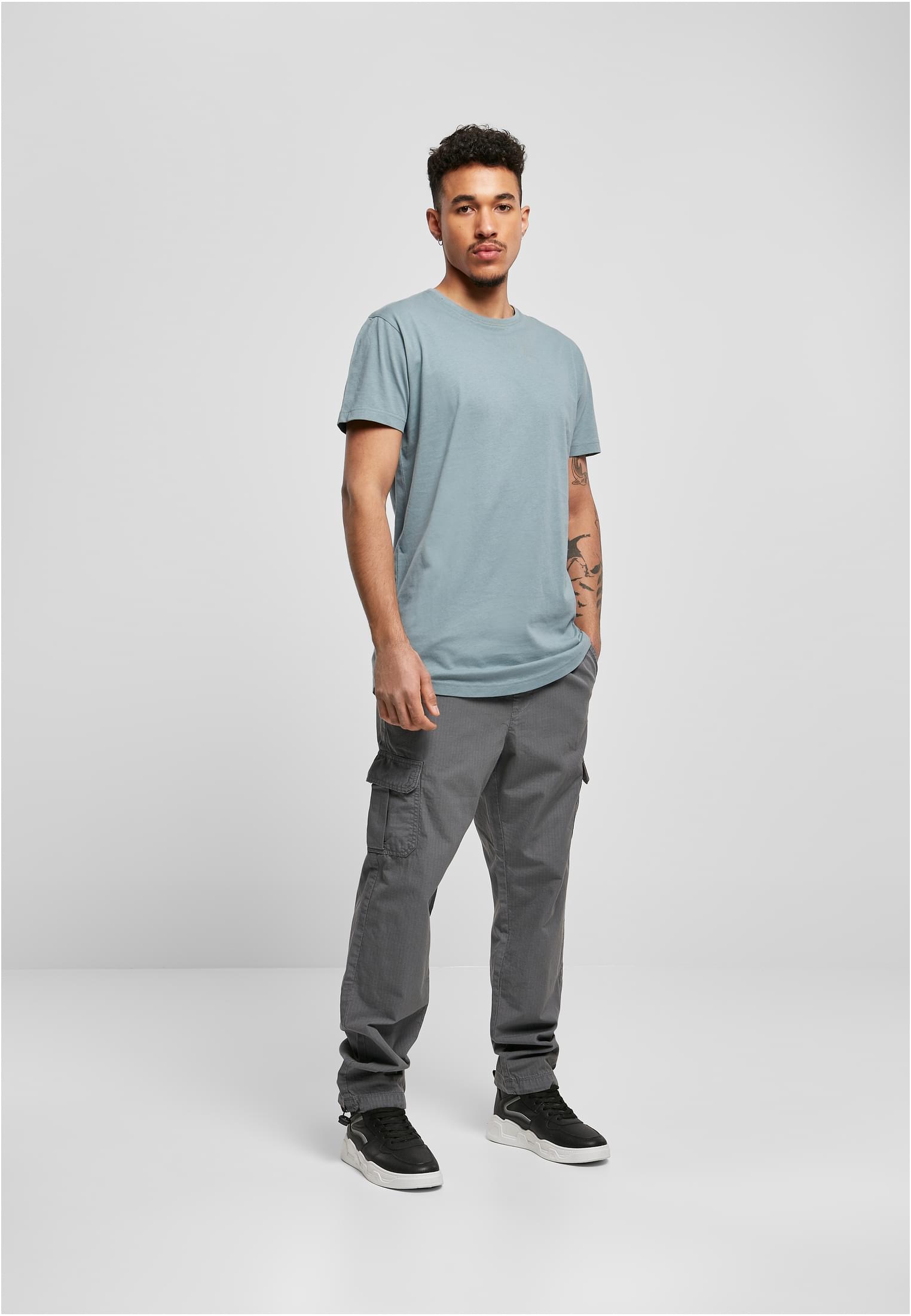 En man som bär en ljusblå UC Shaped Long Tee, grå cargobyxor och svarta sneakers.