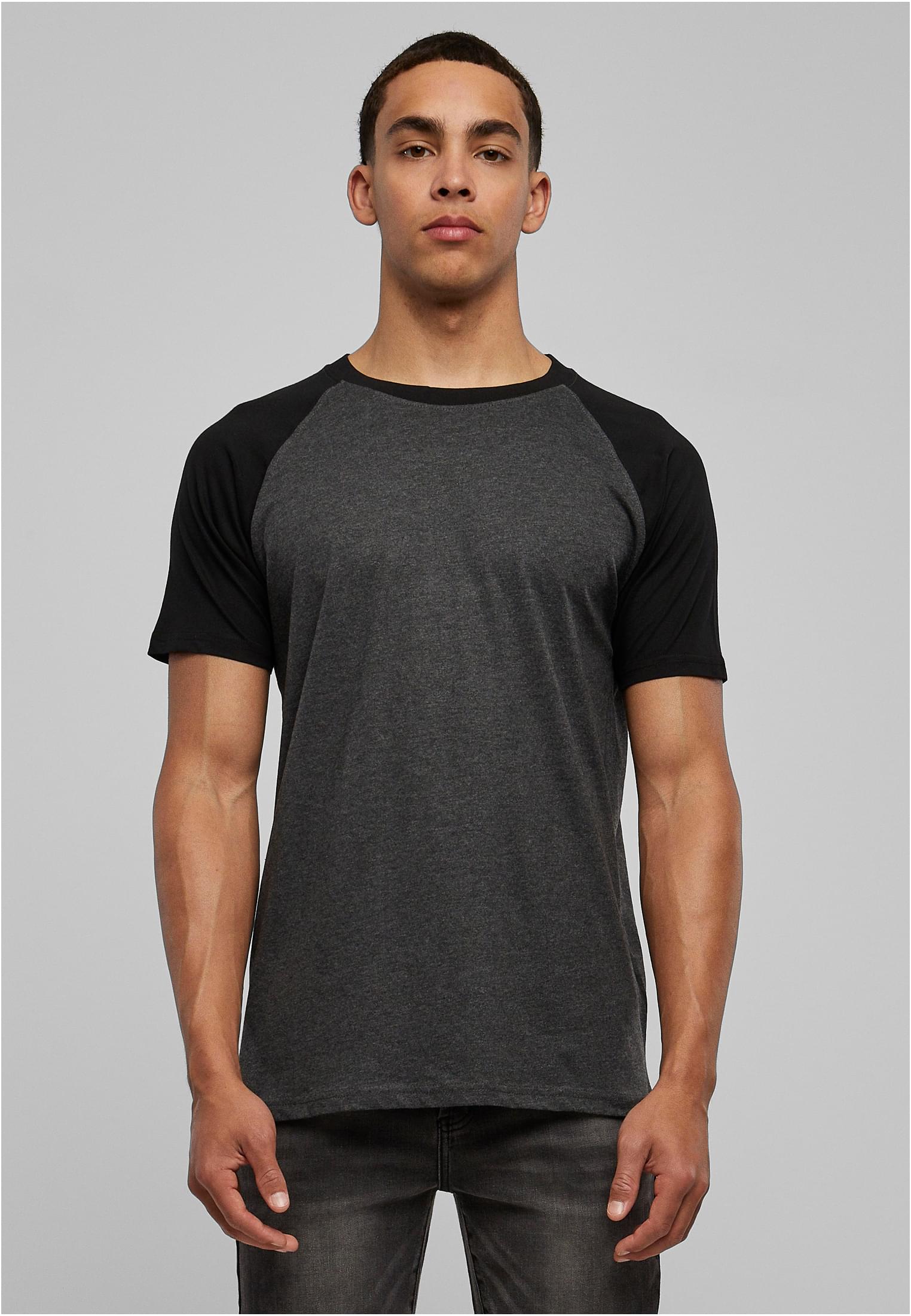 En man poserar framifrån i en mörkgrå t-shirt med svarta raglanärmar.