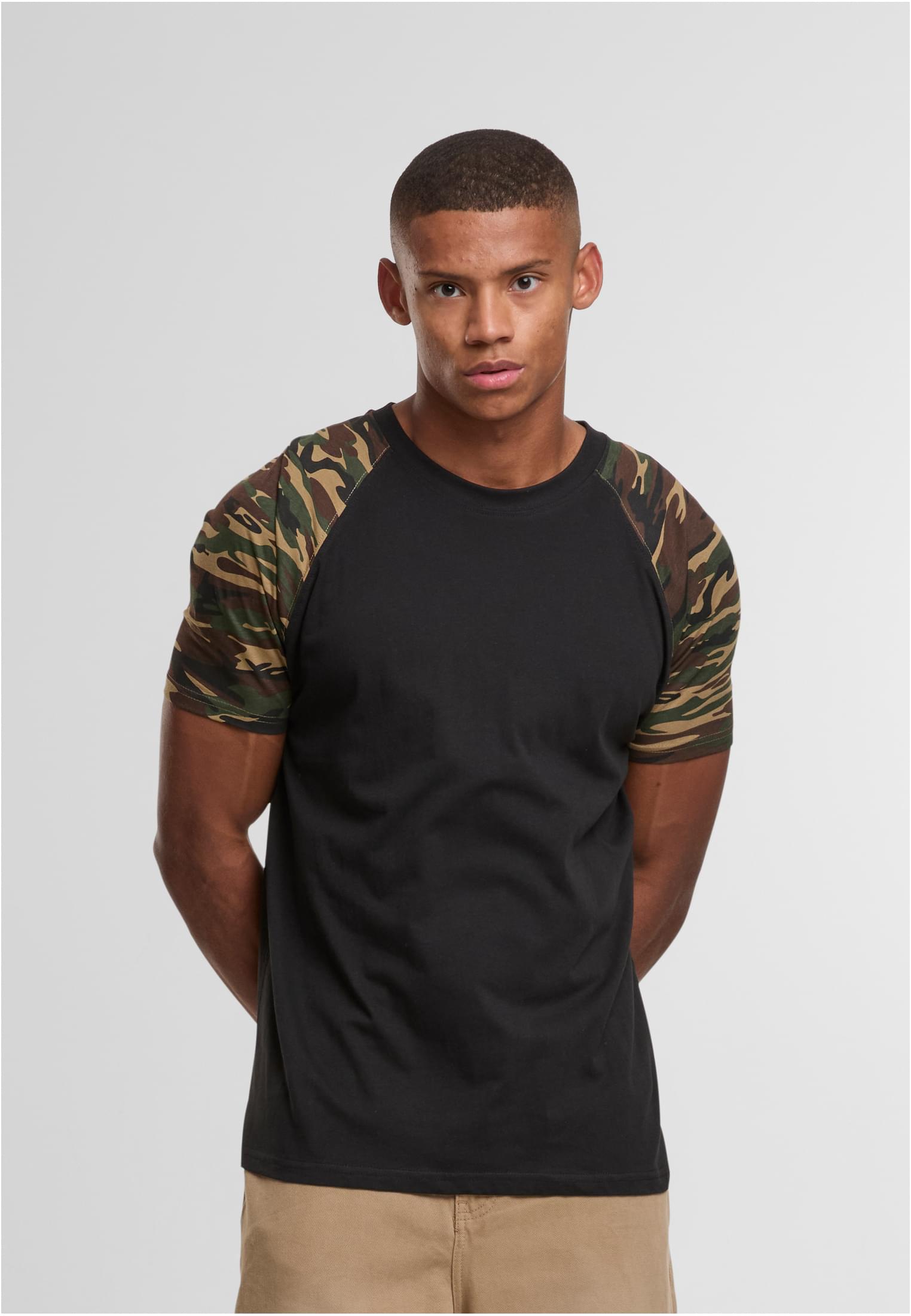 Manlig modell som bär en Raglan Contrast Tee i svart med kamouflagemönstrade ärmar.