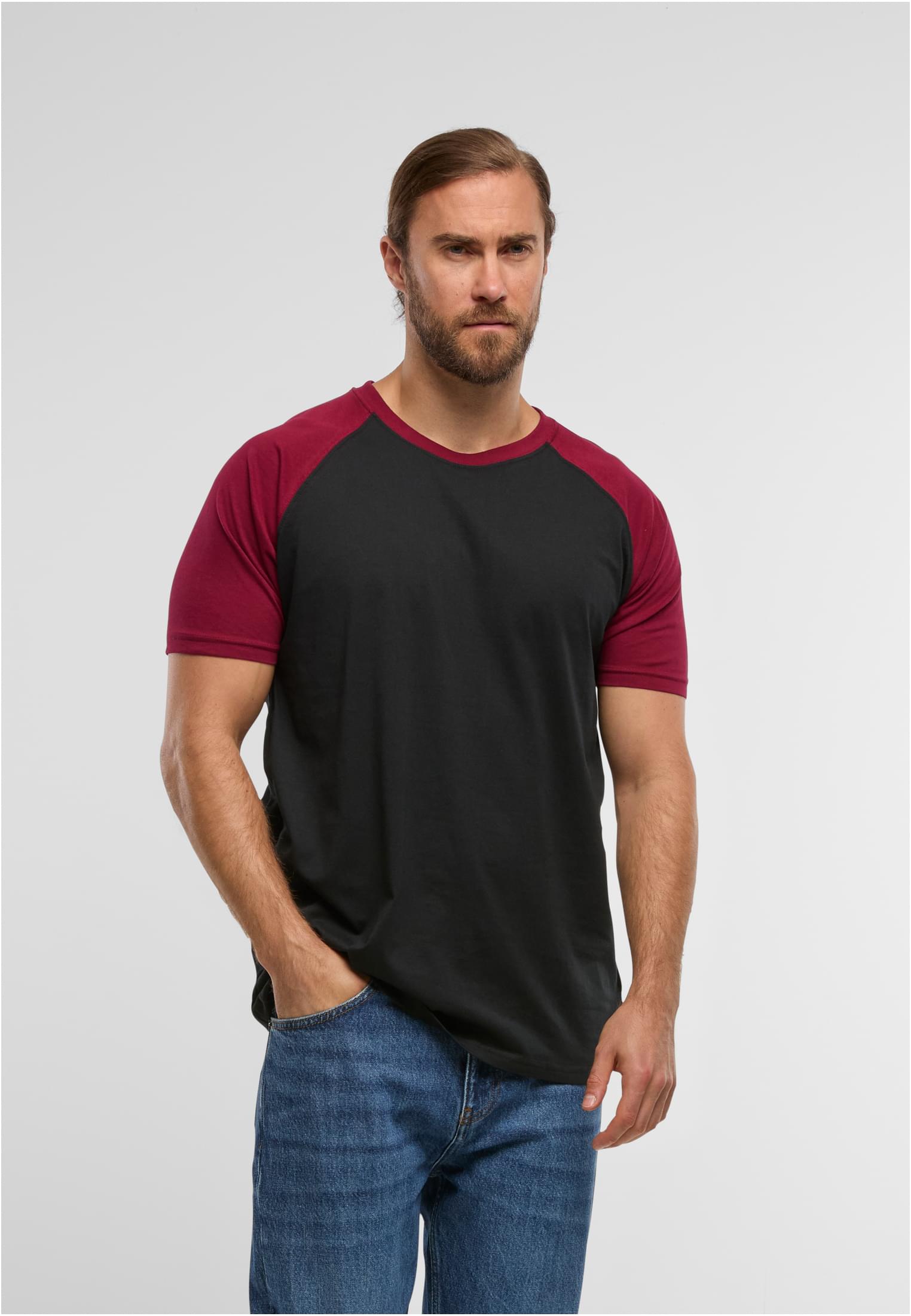 En man poserar i en svart t-shirt med vinröda raglanärmar och blå jeans.