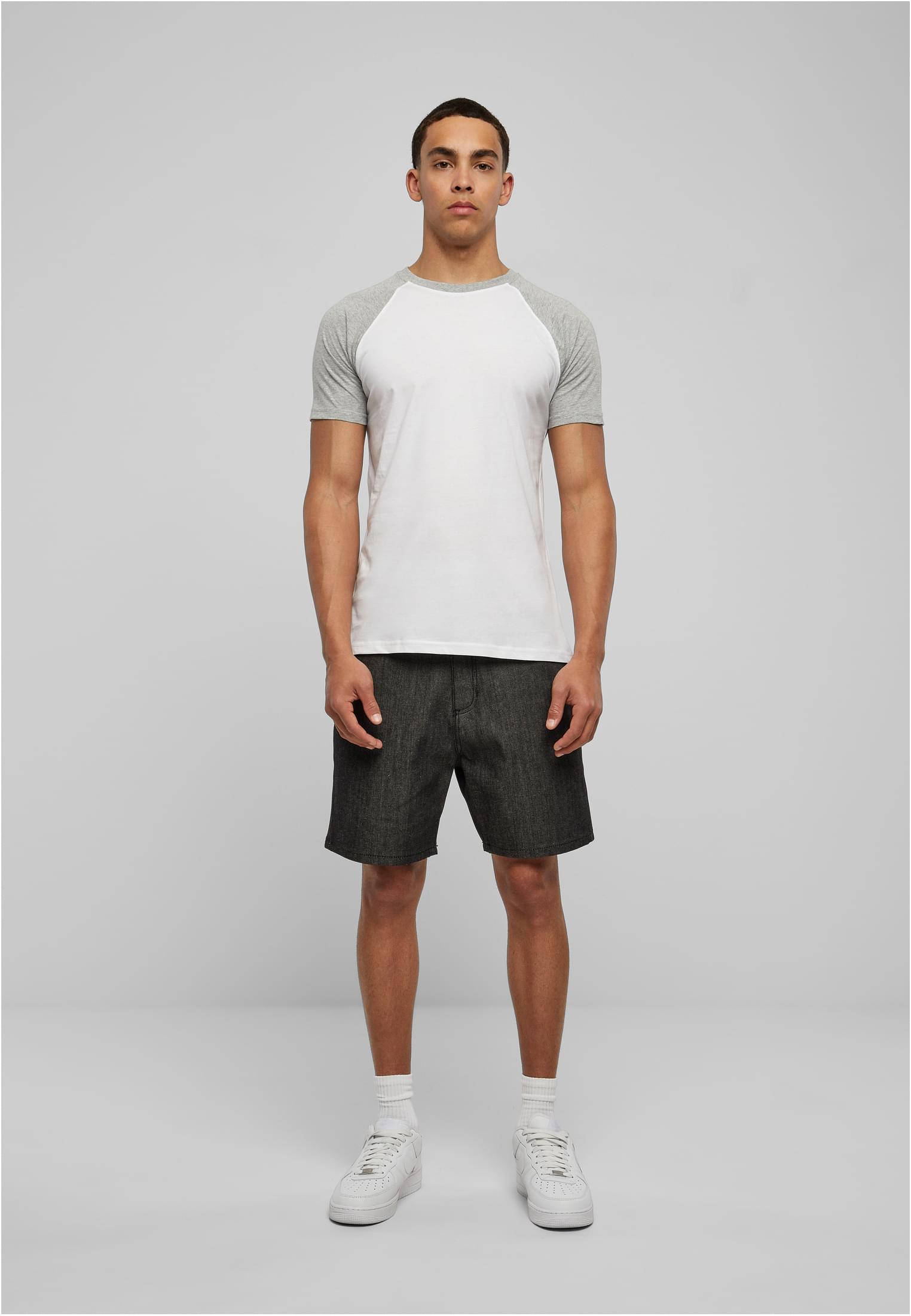 Helbild framifrån av en man som bär en vit och grå Raglan Contrast Tee, mörka shorts och vita sneakers.