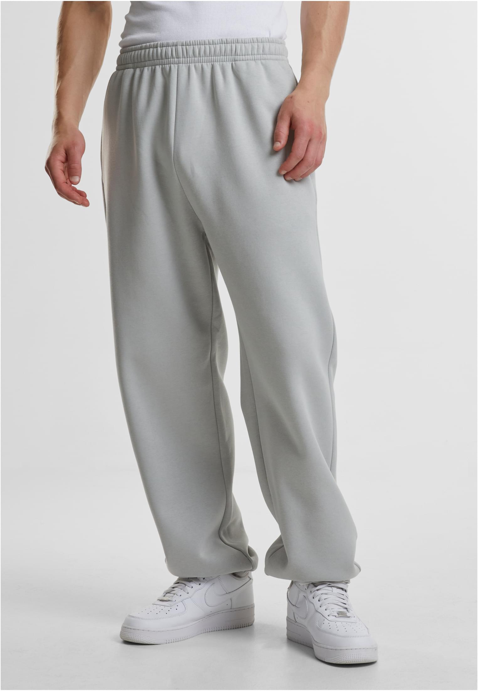 En man bär ljusgrå Fluffy Sweatpants från Urban Classics. Bilden är en närbild från midjan och ner som visar byxornas avslappnade passform.