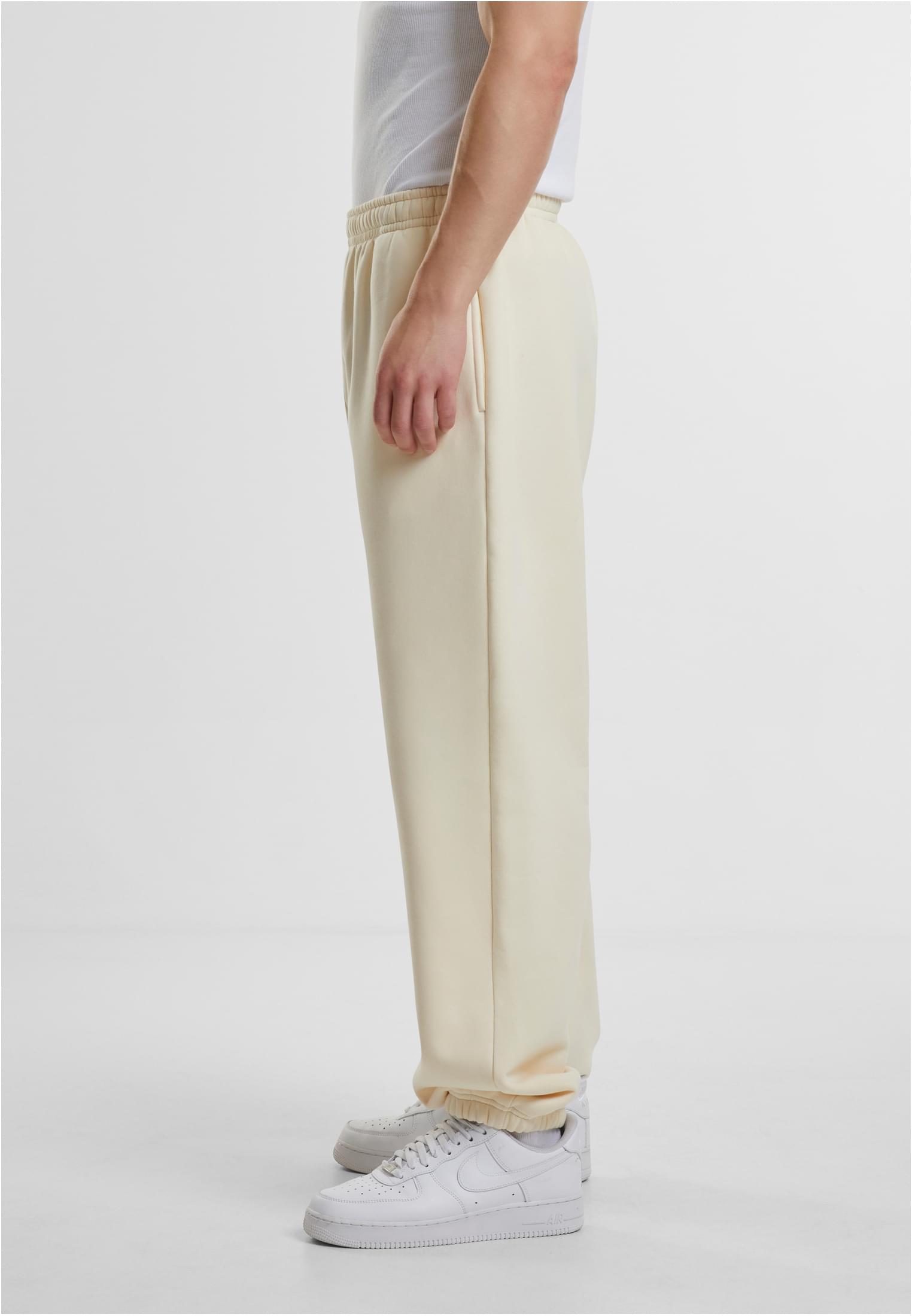 En man fotograferad från sidan som bär ett par benvita Fluffy Sweatpants, ett vitt linne och vita sneakers.