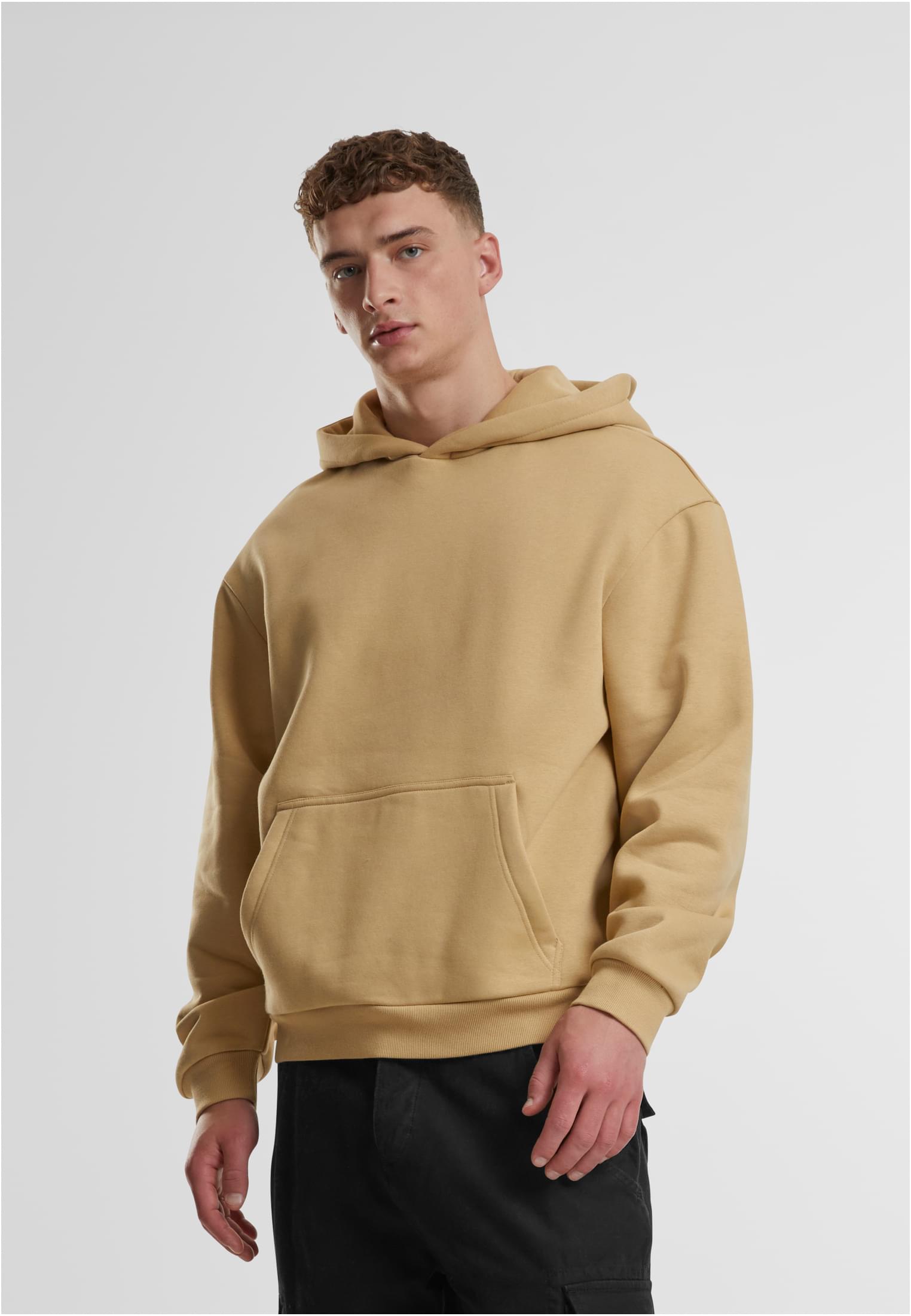 En manlig modell poserar i en beige Fluffy Hoody från Urban Classics.