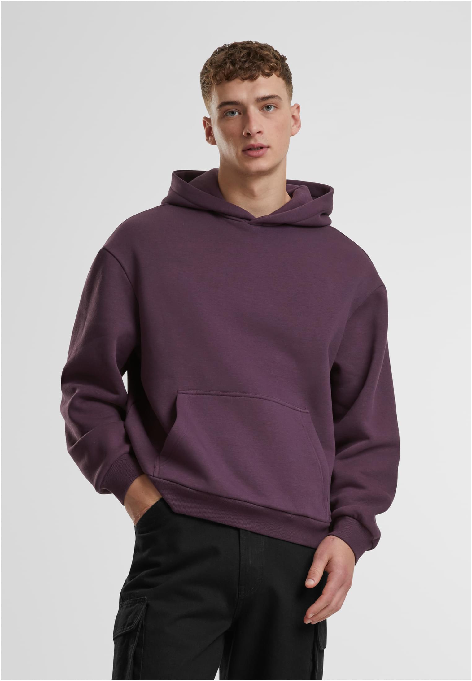 En manlig modell bär en lila Fluffy Hoody från Urban Classics mot en vit bakgrund.