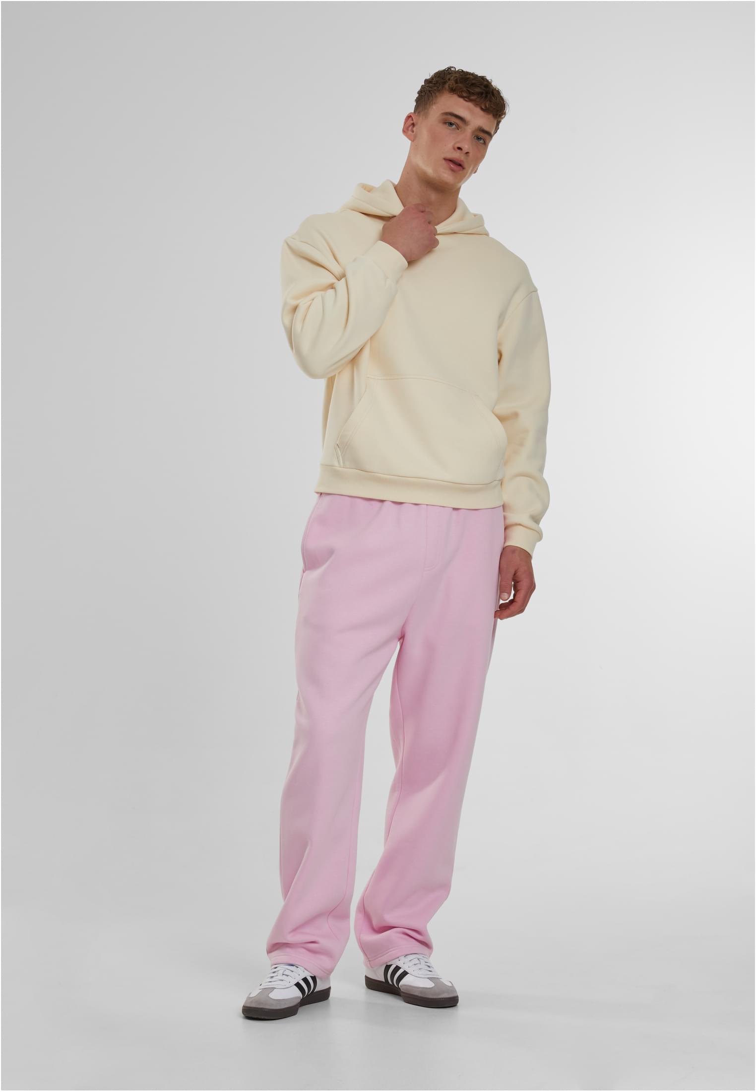 En manlig modell poserar i en krämfärgad Fluffy Hoody och rosa byxor mot en ljusgrå bakgrund.