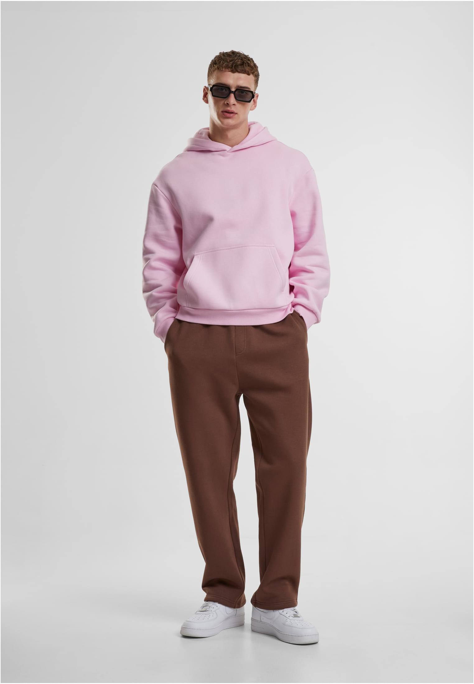 Helbild på en man som bär en ljusrosa Fluffy Hoody från UC Men, bruna byxor och vita sneakers.