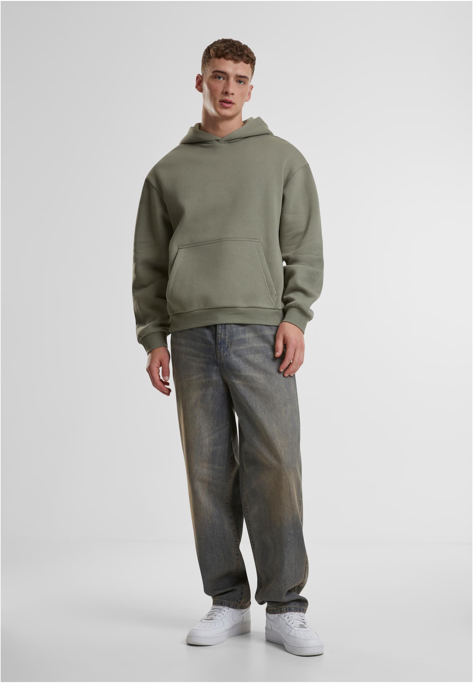 Manlig modell i en grön Fluffy Hoody, vida jeans och vita sneakers.