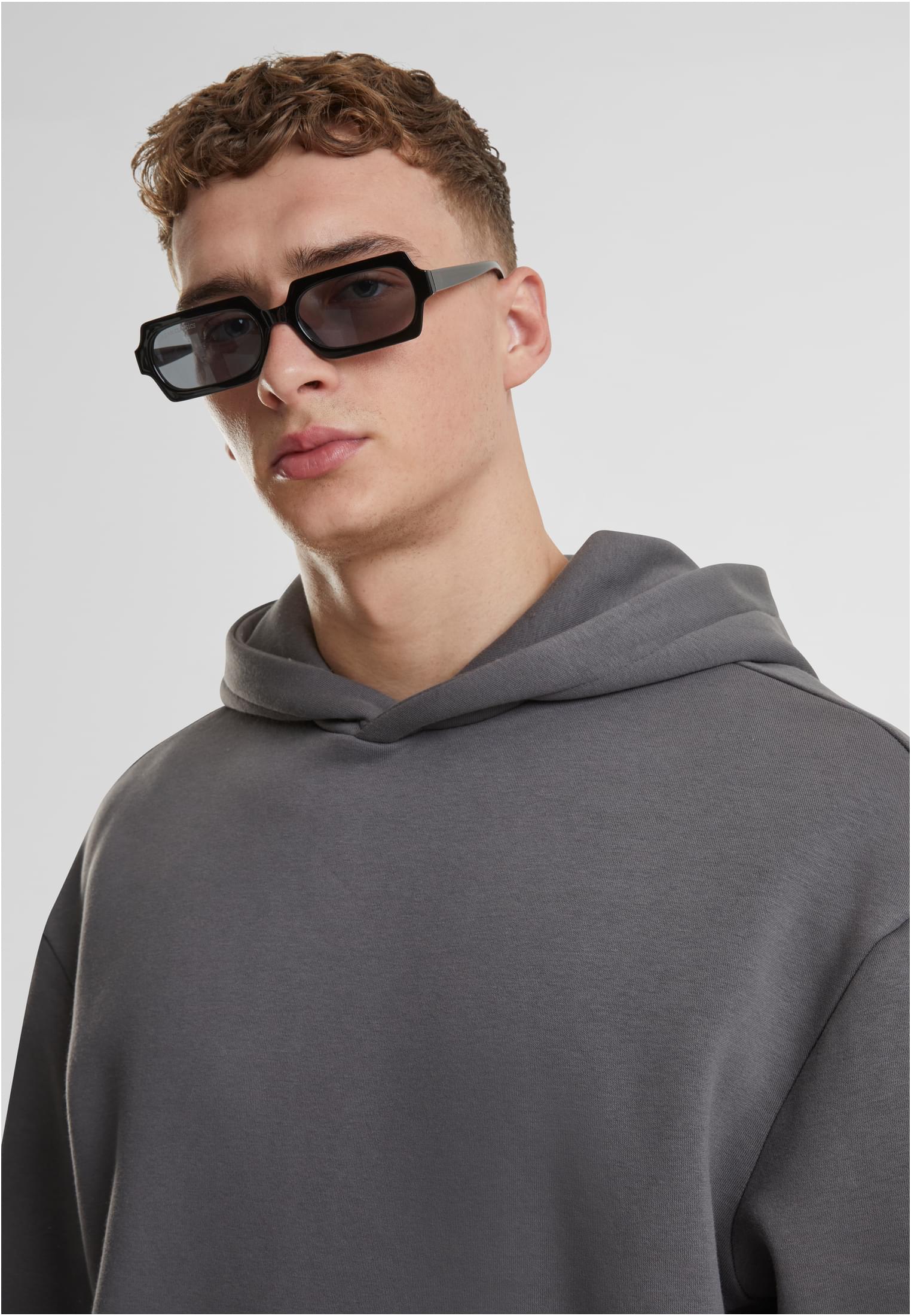 Närbild på en man som bär en grå luvtröja och svarta, kantiga solglasögon.