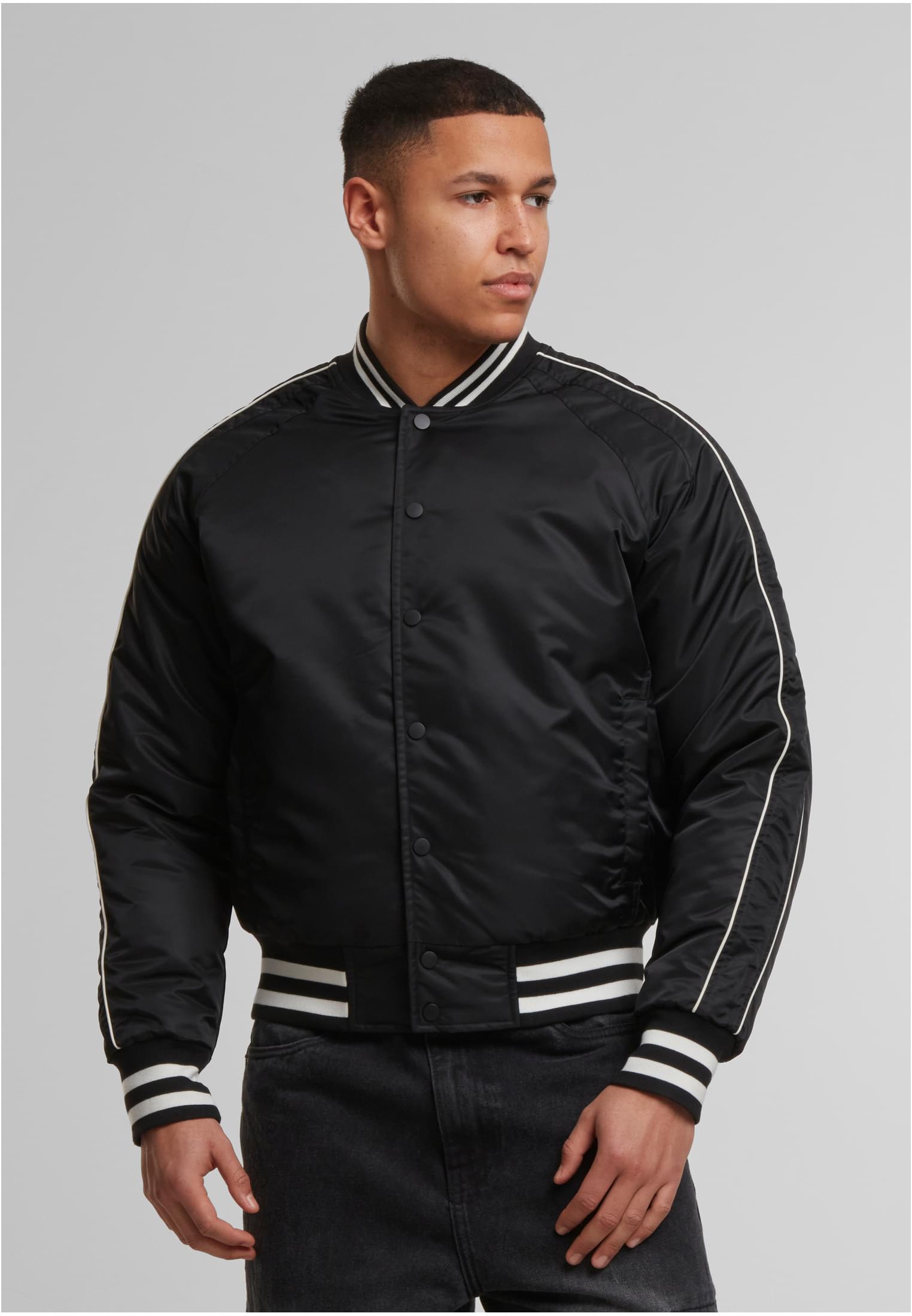 En man poserar i en svart UC Racer Bomber Jacket med vita ränder på kragen, muddarna och midjebandet.
