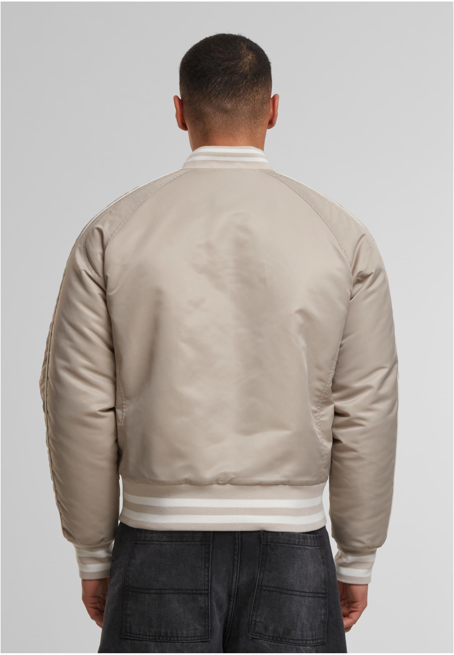 En man visar baksidan av en beige UC Racer Bomber Jacket med randiga muddar.