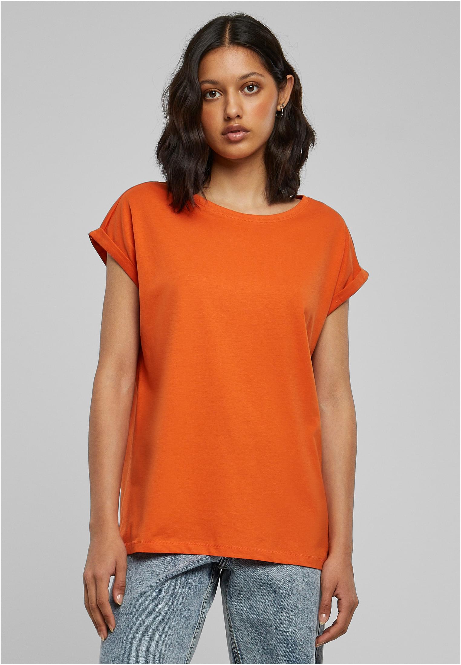 En kvinna som modellar en orange t-shirt med nedhasade axlar och uppvikta ärmar.