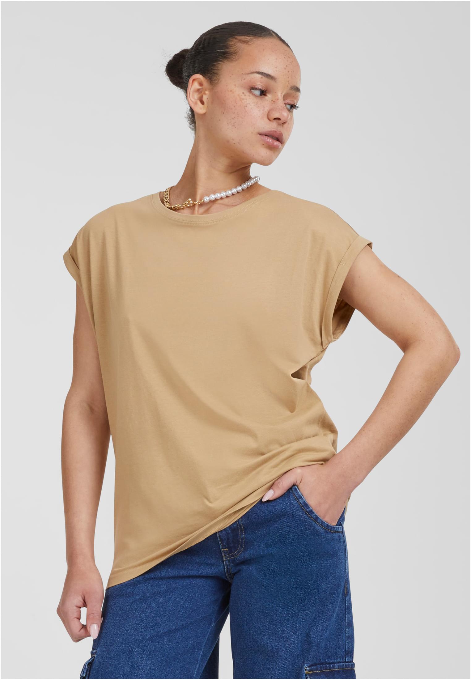 Kvinna som bär en beige Ladies Extended Shoulder Tee med nedhasade axlar och uppvikta ärmar, stylad med blå jeans och ett halsband.