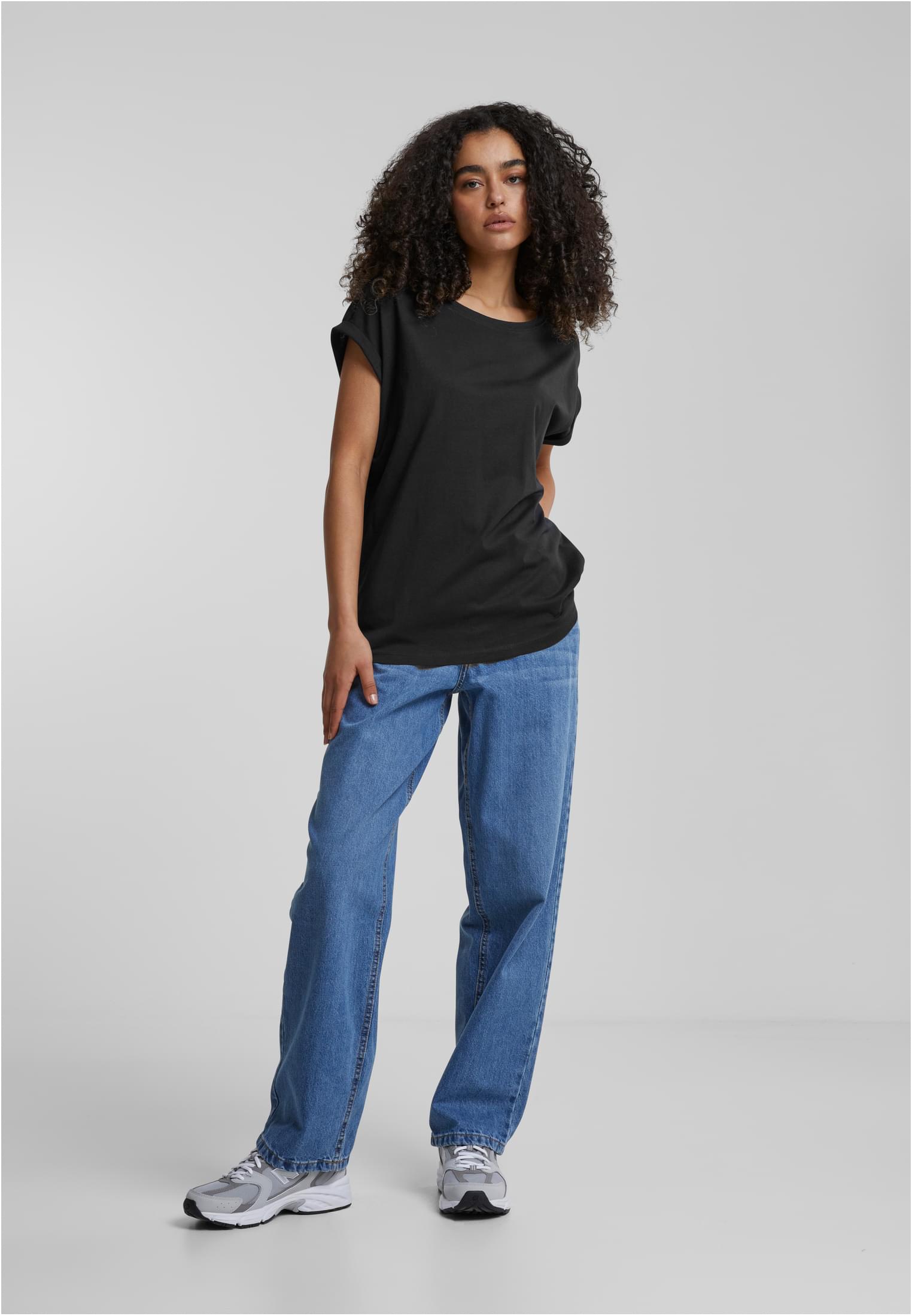 Framsida på en modell som bär en mörk t-shirt för damer med förlängda axlar, kombinerad med ljusblå jeans och sneakers.
