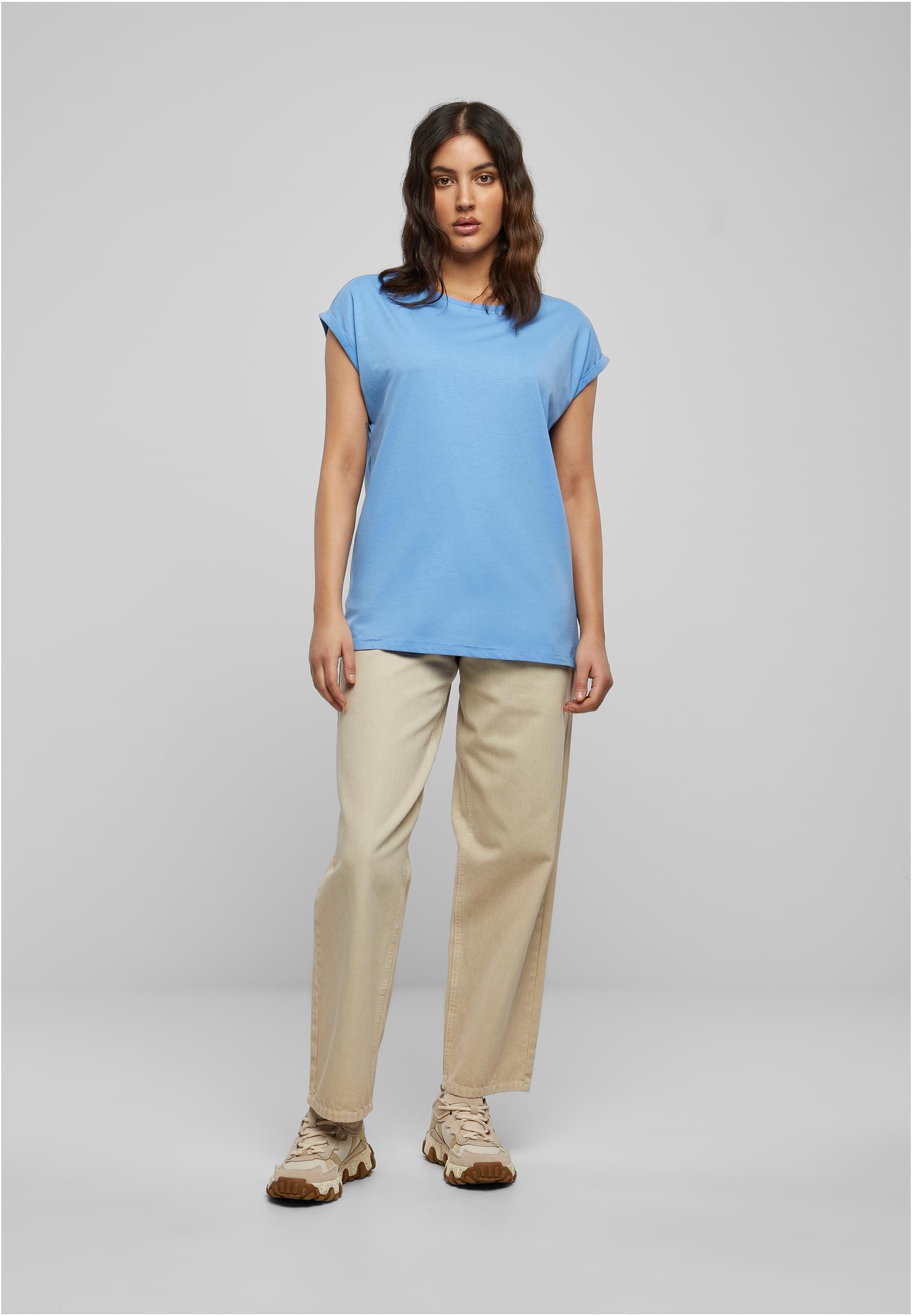 Kvinna som bär en ljusblå t-shirt med nedhasade axlar och uppvikta ärmar, stylad med vida beiga byxor och sneakers.