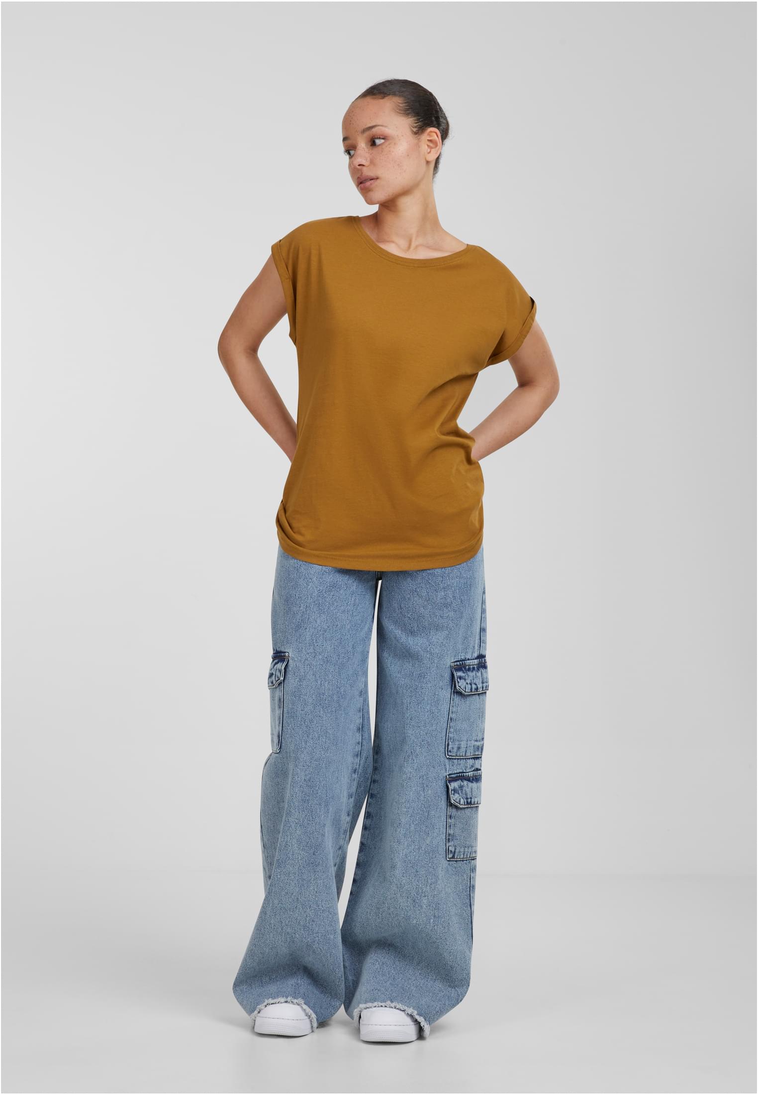 En modell visar en Ladies Extended Shoulder Tee, en t-shirt med nedhasade axlar och uppvikta ärmar. Hon har på sig vida jeans och poserar mot en ljusgrå bakgrund.