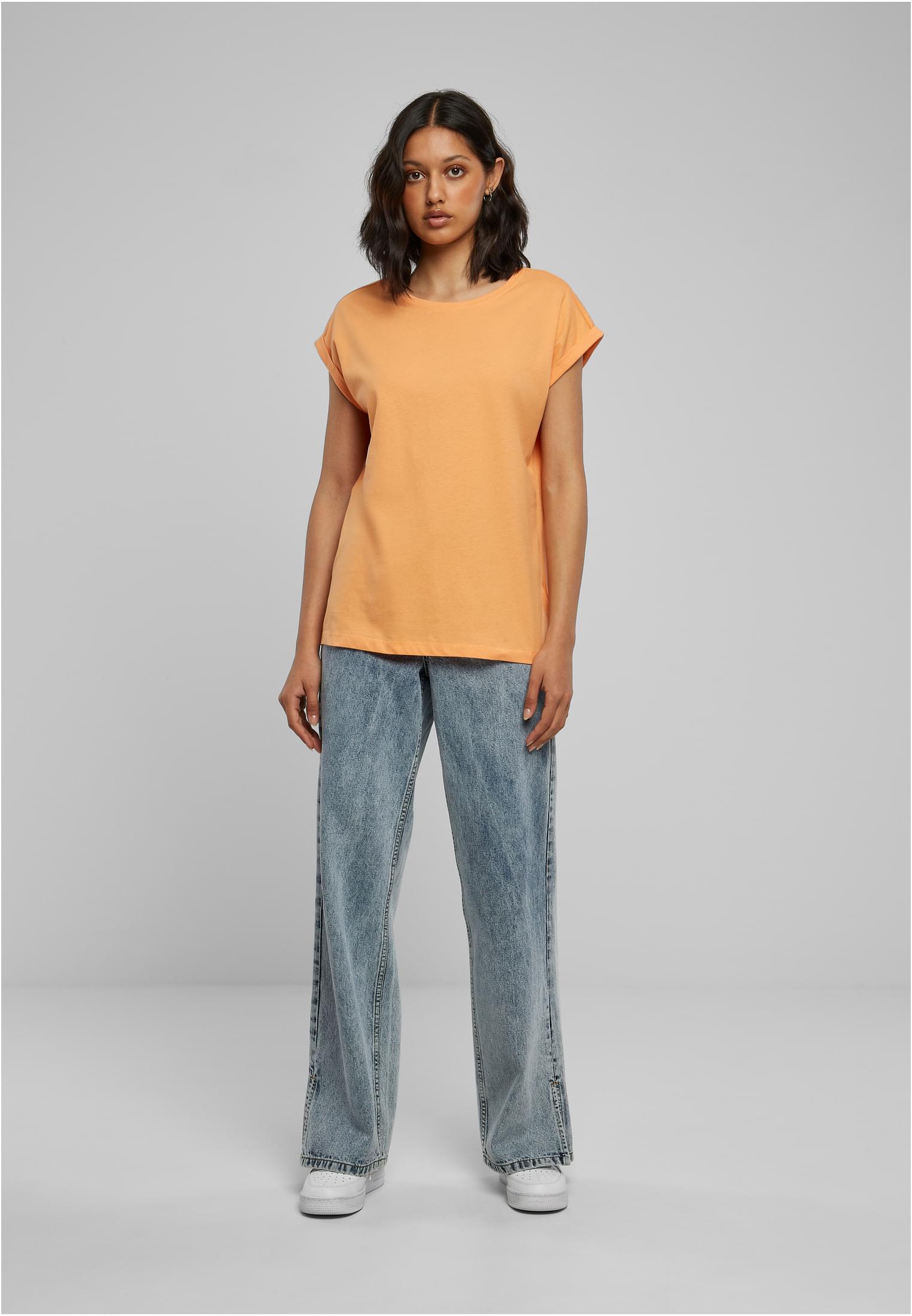 Kvinna i en persikofärgad t-shirt med nedhasade axlar, stylad med vida ljusblå jeans och vita sneakers.