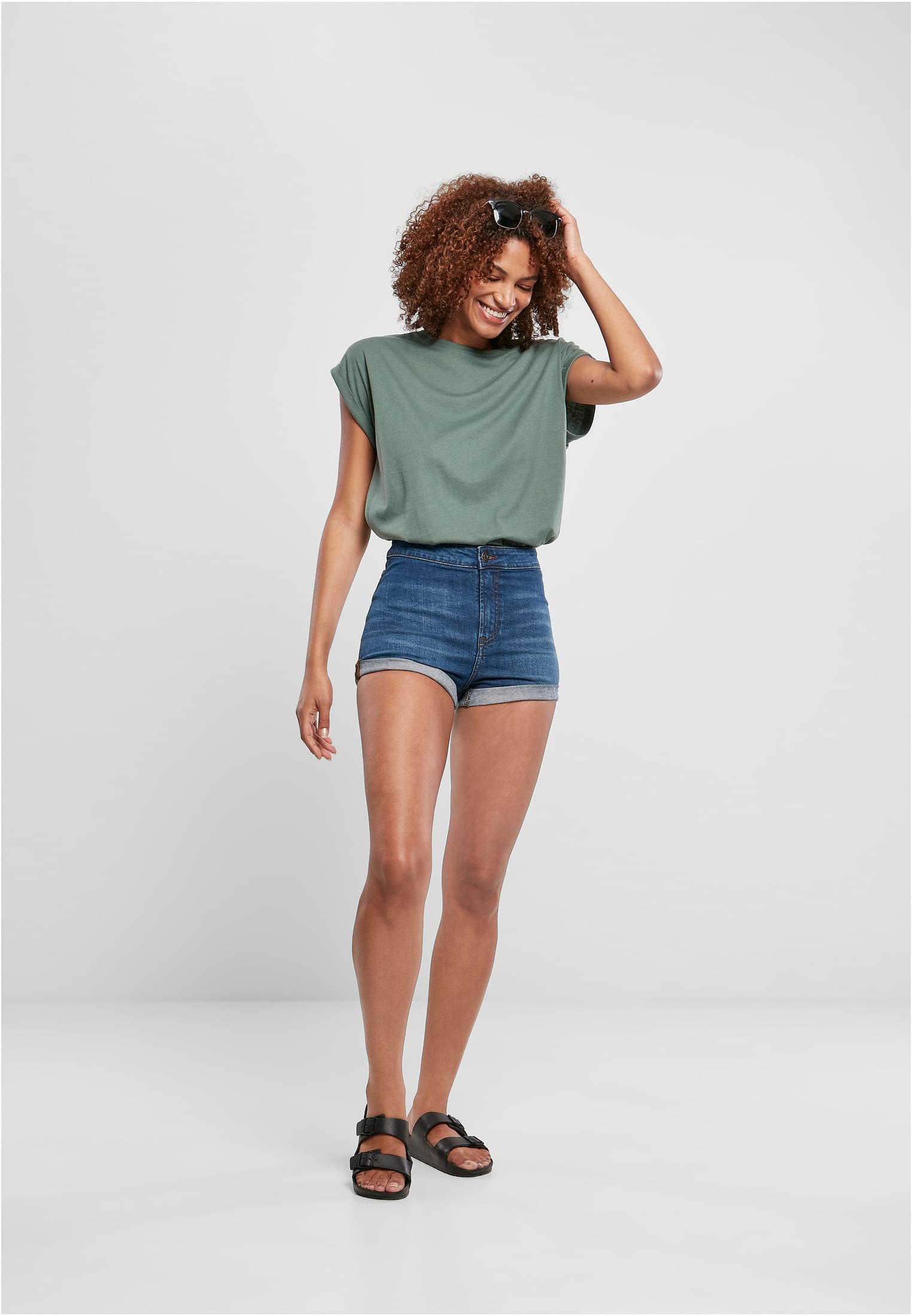 En helkroppsbild på en leende kvinna som bär en mintgrön Ladies Extended Shoulder Tee, instoppad i blåa jeansshorts och stylad med svarta sandaler.