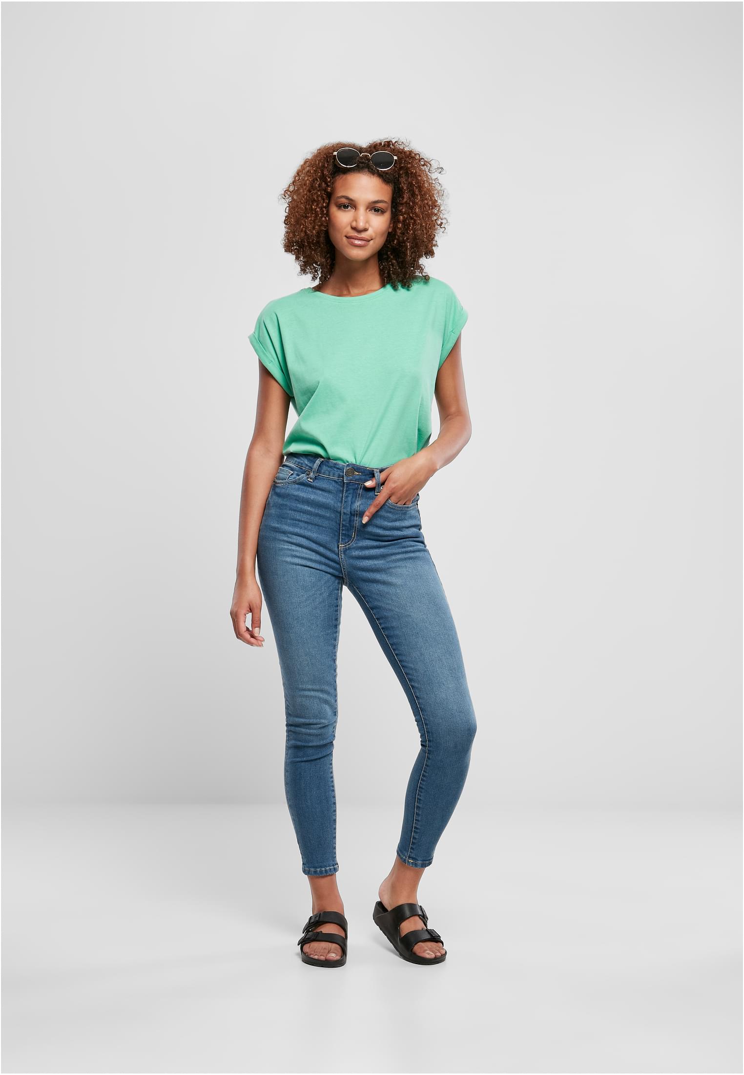 Kvinna i helfigur som bär en mintgrön Ladies Extended Shoulder Tee, stylad med blå jeans och svarta sandaler.