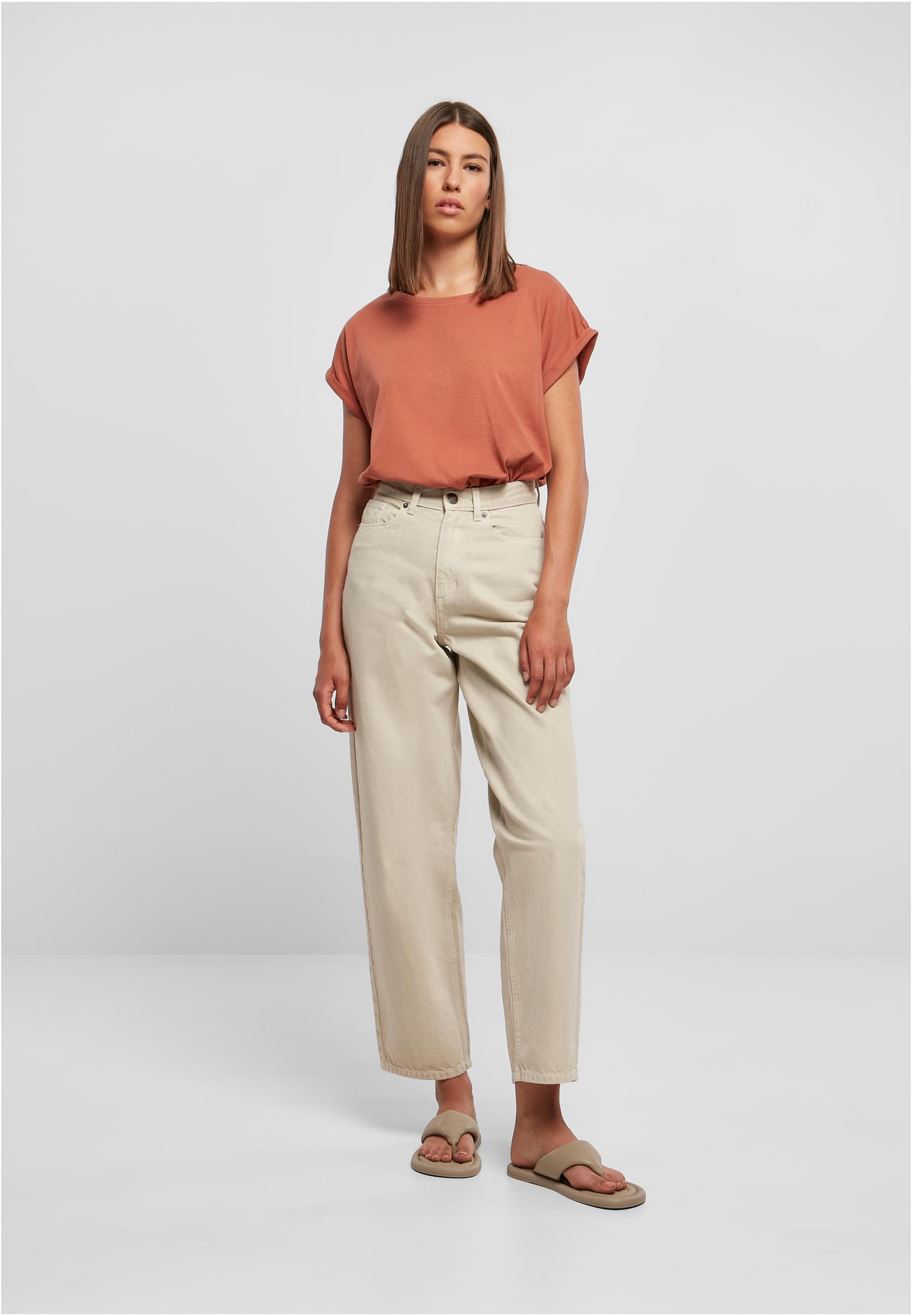 En kvinna som bär en rostfärgad Ladies Extended Shoulder Tee med beigefärgade byxor och sandaler.