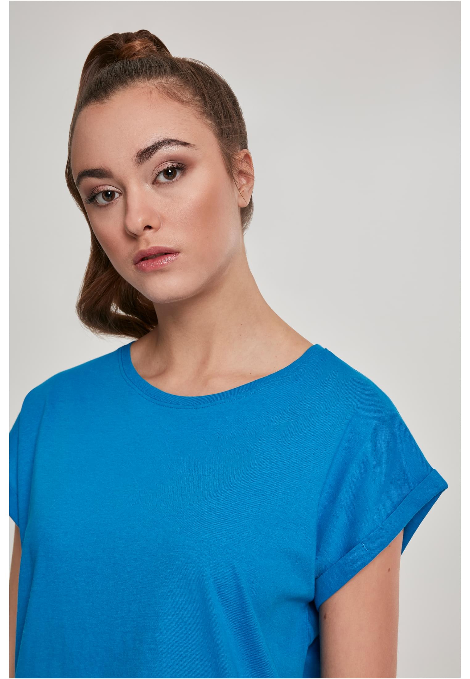 Närbild på en kvinna som bär en blå UC Ladies Extended Shoulder Tee med uppvikta ärmar.