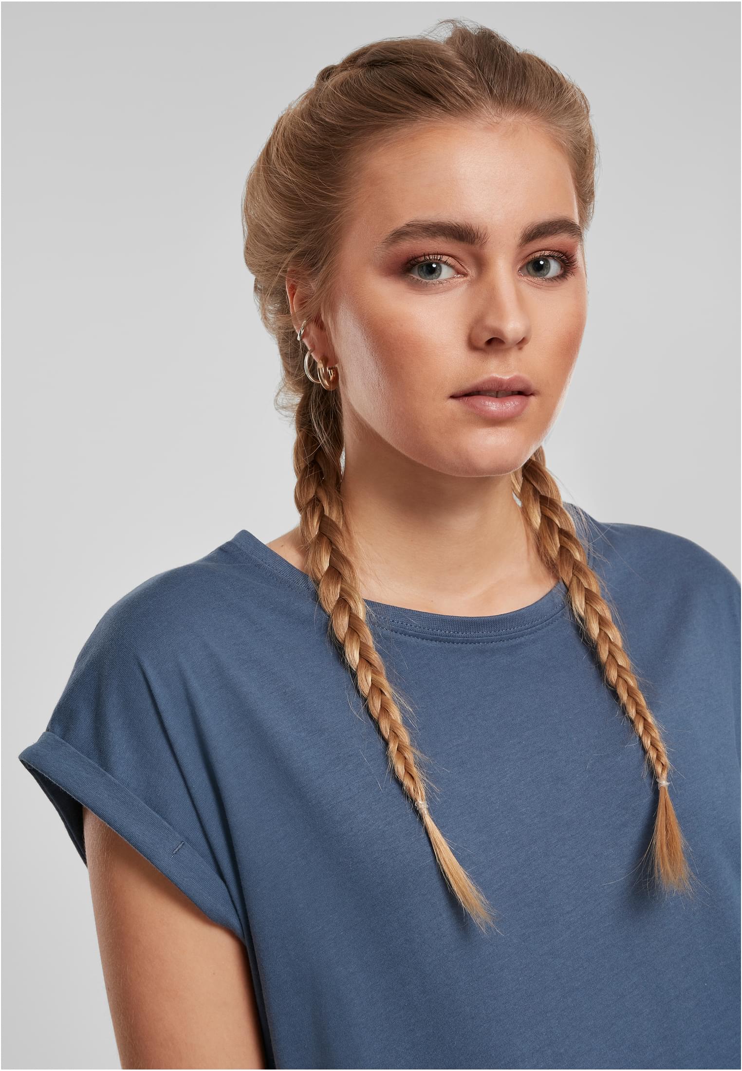Närbild på en kvinna med blont hår i flätor som bär en blågrön Ladies Extended Shoulder Tee.