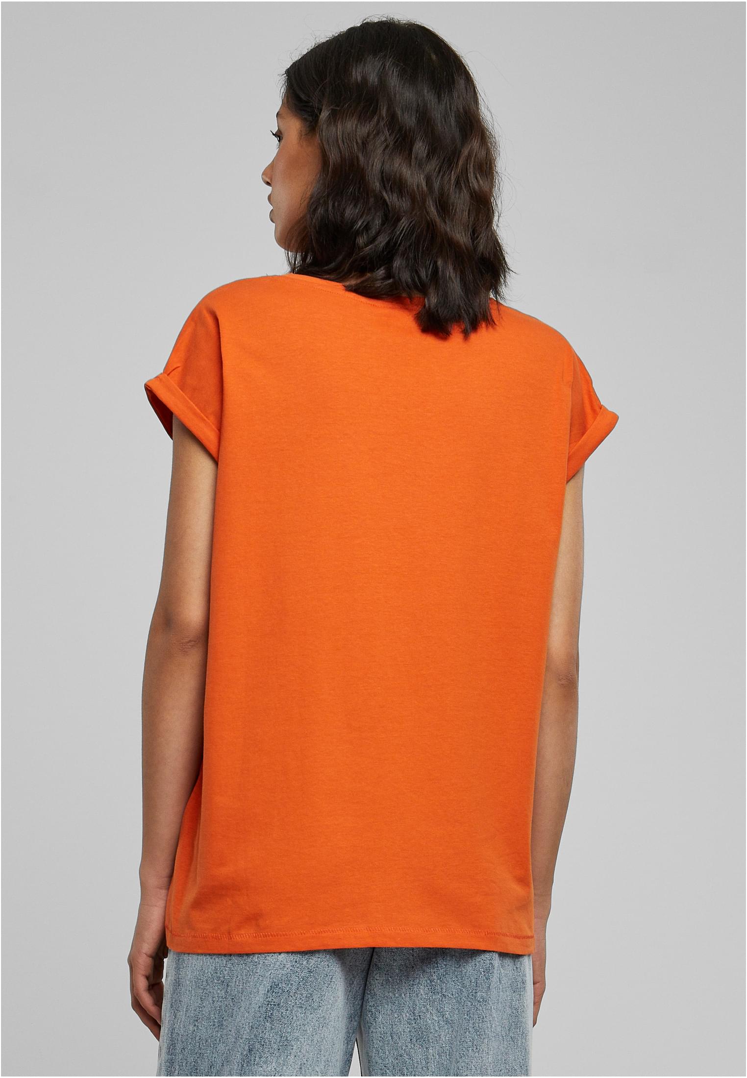 Kvinna fotograferad bakifrån, klädd i en orange UC Ladies Extended Shoulder Tee med uppvikta ärmar.