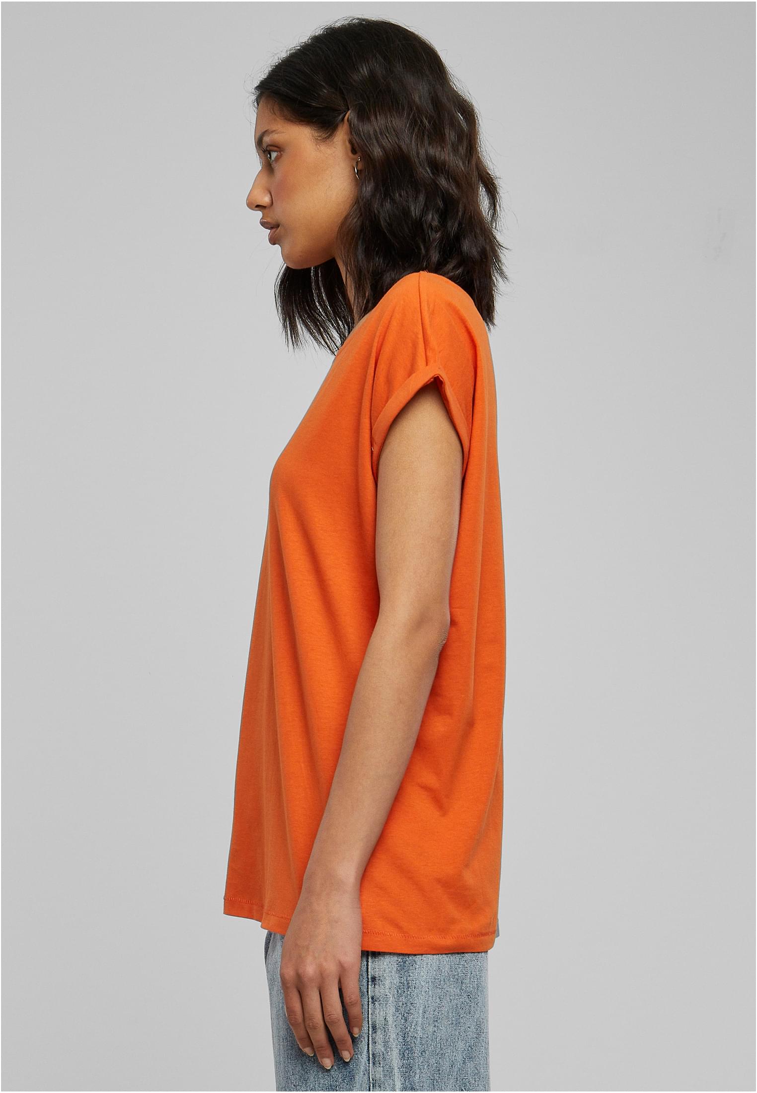 Sidovy av en kvinna som bär en orange UC Ladies Extended Shoulder Tee med nedhasade axlar och uppvikta ärmar.
