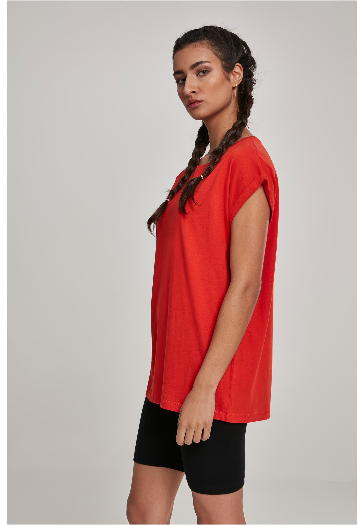 Sidovy av en kvinna med flätat hår som bär en röd, ledig t-shirt med uppvikta ärmar och svarta cykelbyxor.