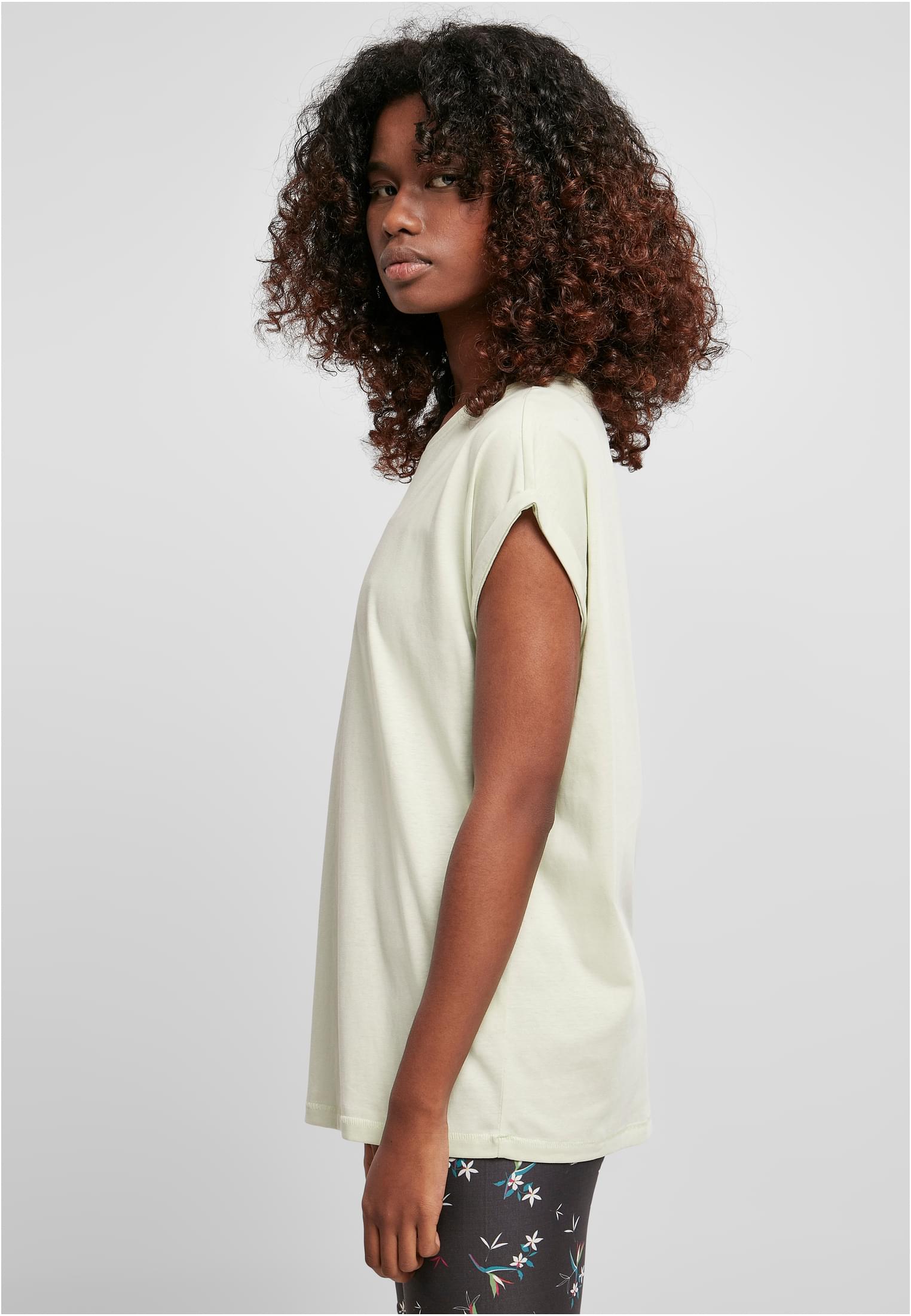 En kvinna med lockigt hår, fotograferad från sidan, bär en mintgrön t-shirt med nedhasade axlar och uppvikta ärmar.