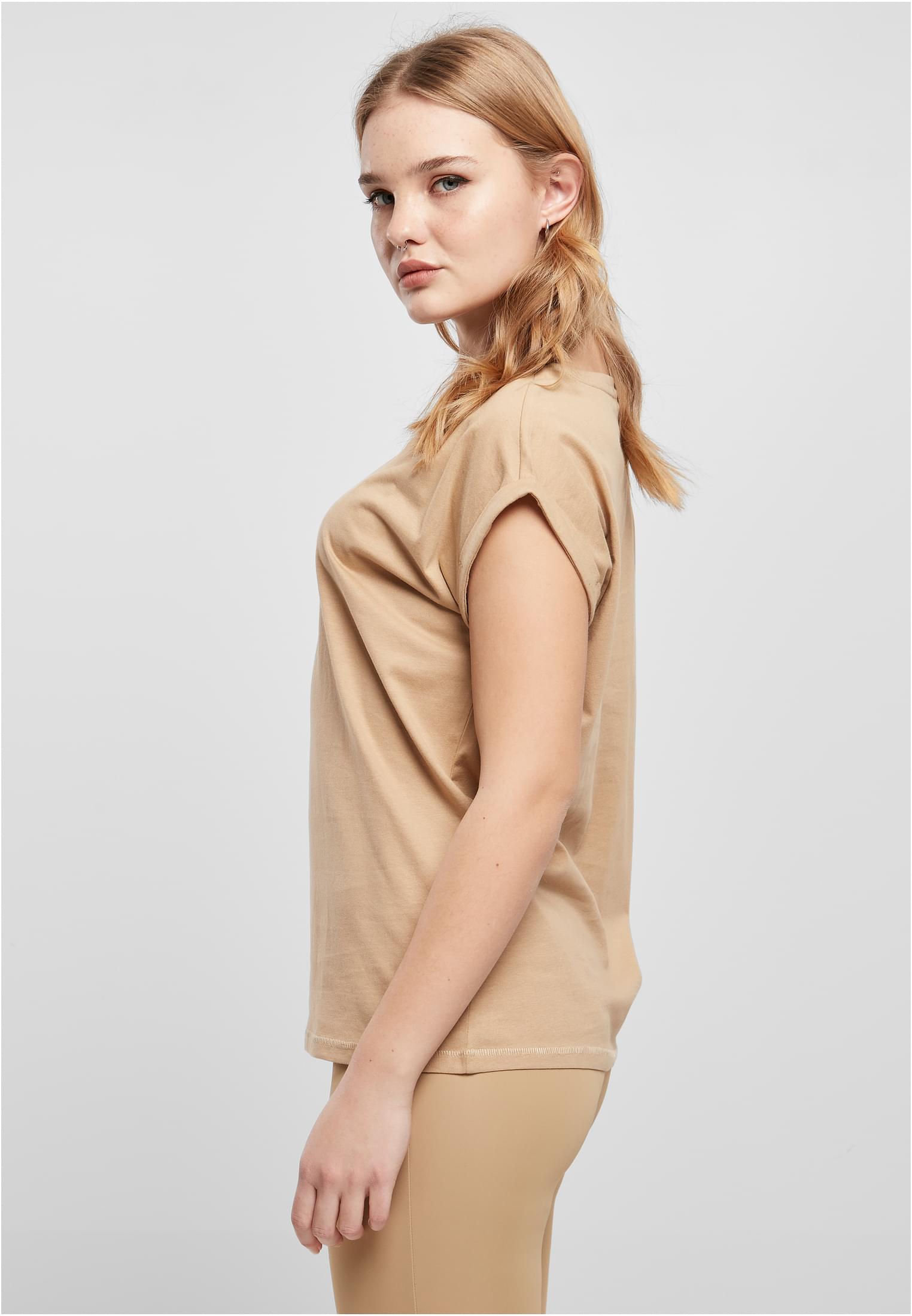 Sidovy av en kvinna som bär en beige Ladies Extended Shoulder Tee med nedhasade axlar och uppvikta ärmar.