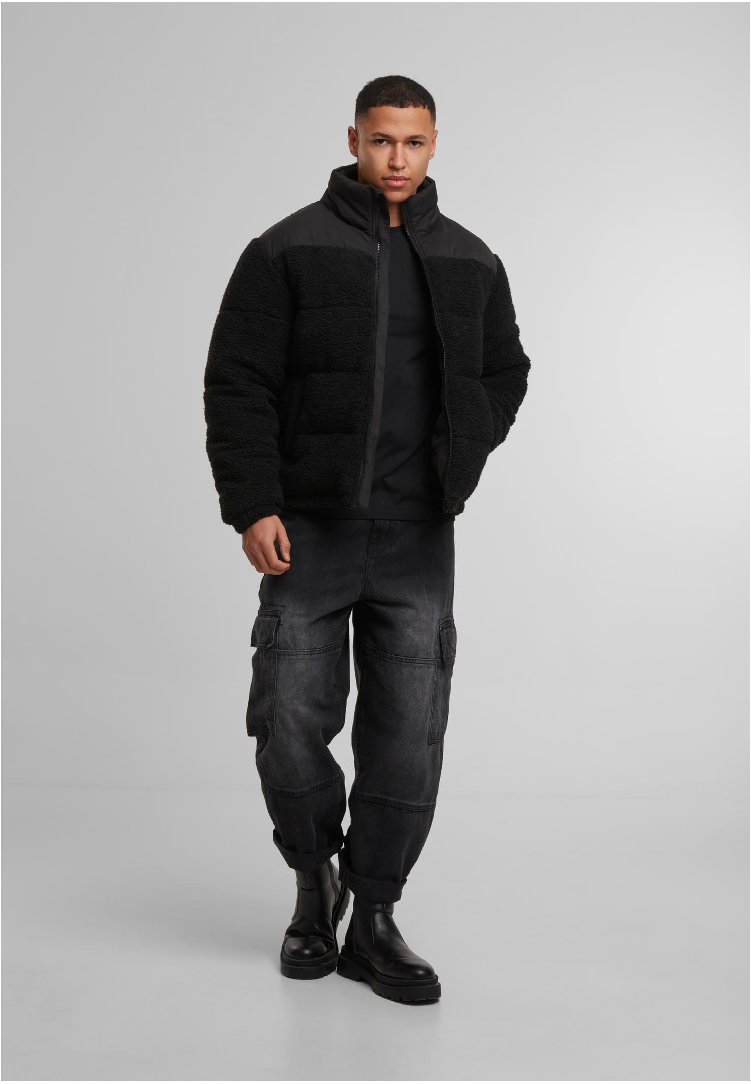 En manlig modell visar framsidan av en svart teddy-puffjacka, stylad med svarta cargobyxor och svarta kängor, mot en grå bakgrund.
