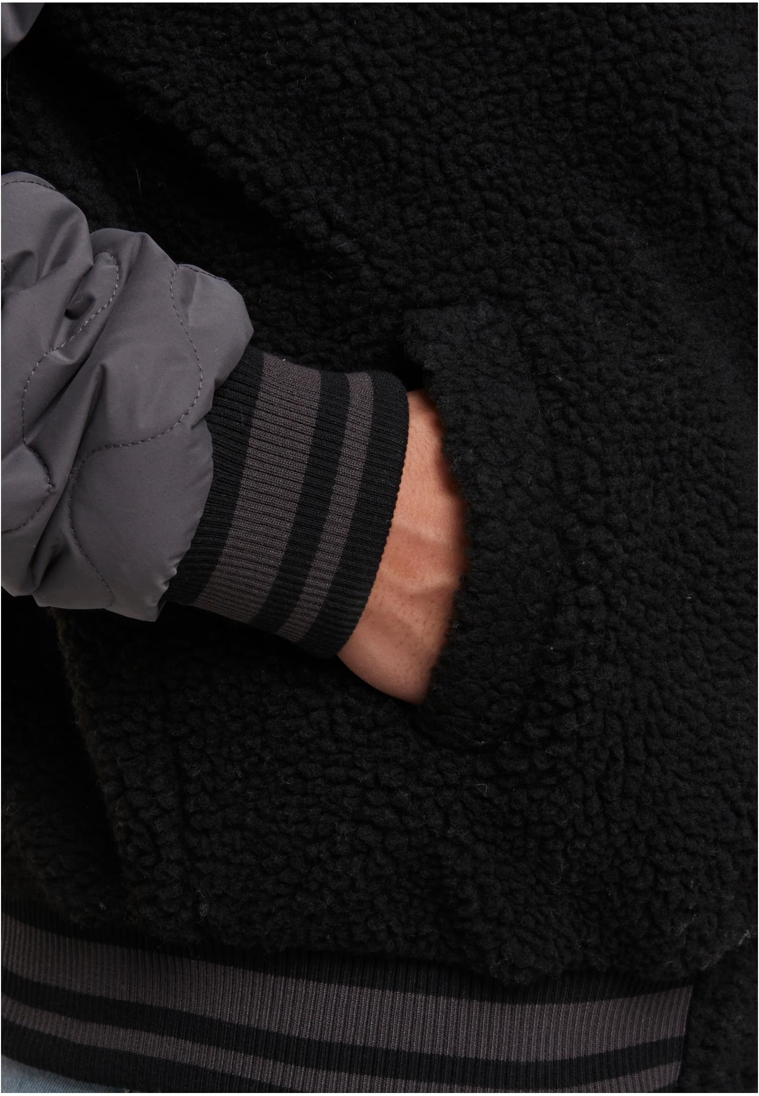 Närbild på en mans hand i fickan på en mörk Teddy College-jacka med randig mudd.