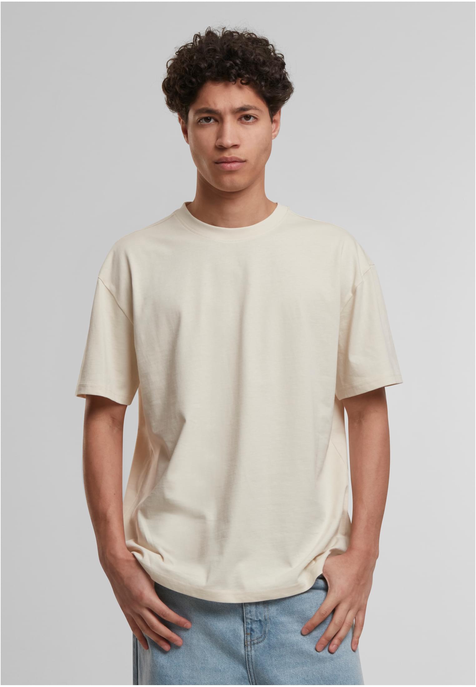 En manlig modell som bär en benvit, löst sittande Cotton Loose Tee med händerna i fickorna.