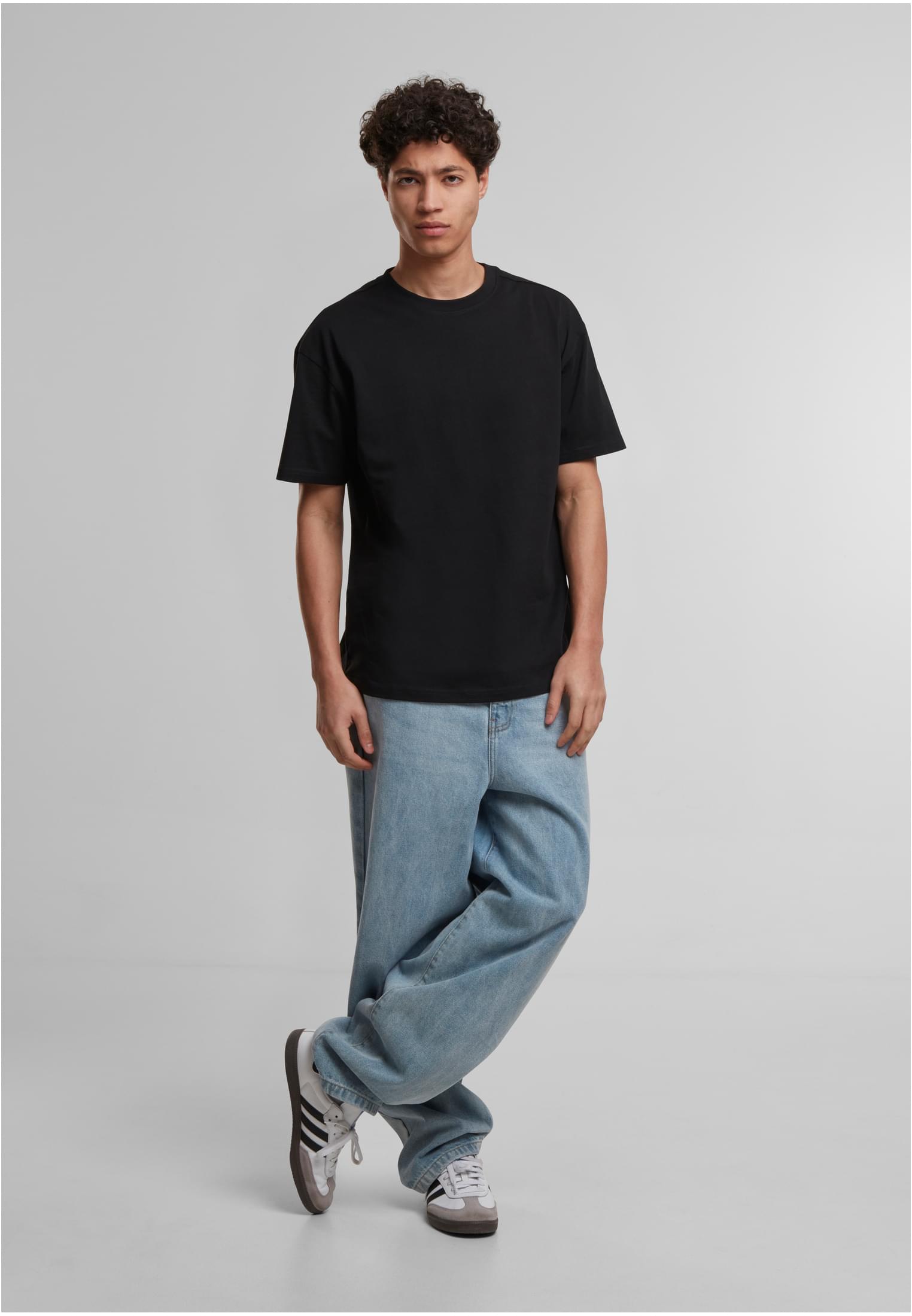 Manlig modell som bär en svart löst sittande t-shirt och ljusblå baggy jeans.