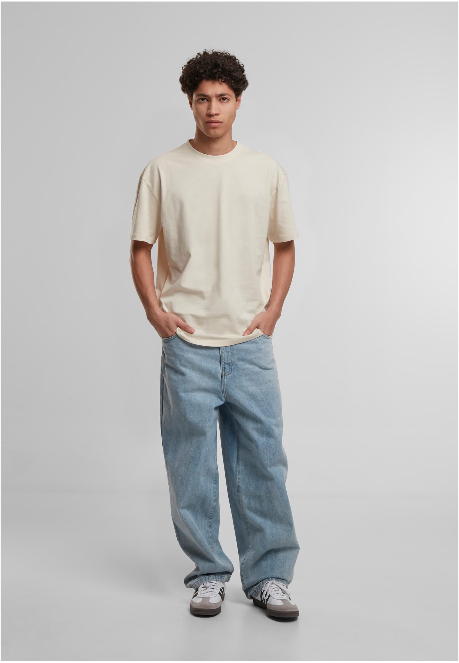 En manlig modell som bär en krämfärgad Cotton Loose T-shirt, ljusblå pösiga jeans och sneakers.