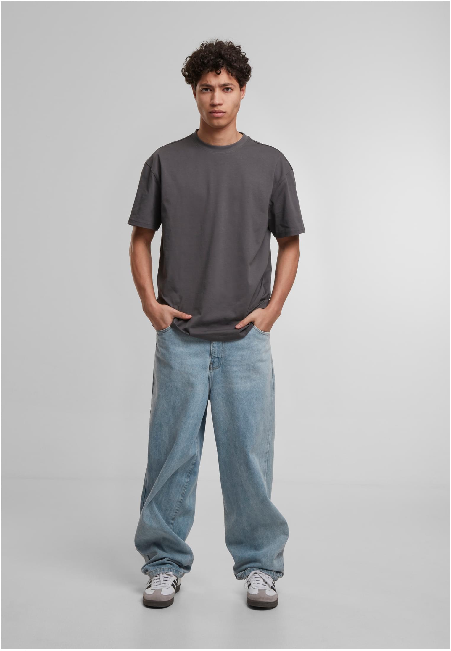En man med en mörkgrå, löst sittande t-shirt och ljusa, vida jeans, fotograferad framifrån.